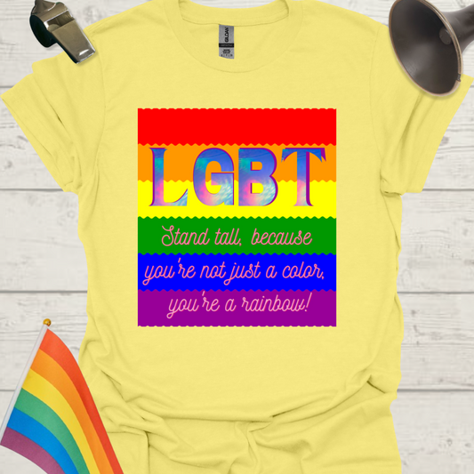 Yellow t-shirt with rainbow-colored 'LGBT' text and motivational quote, displayed on a wooden surface with a rainbow flag and whistle.